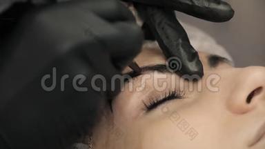 特写，美容师用黑色橡胶的手在眉毛上涂上永久的化妆-眉毛纹身